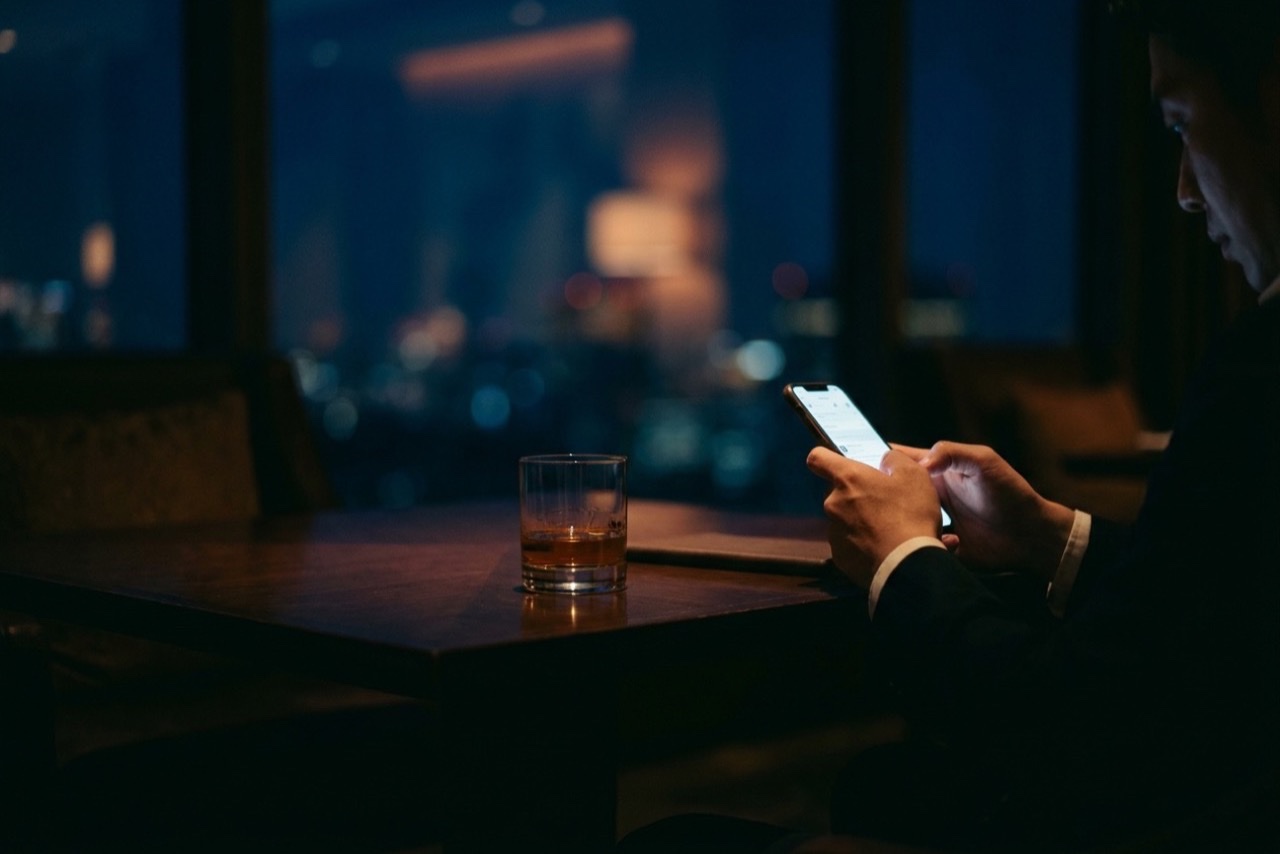 A hand holding a brightly lit phone close to a face in a completely dark room
